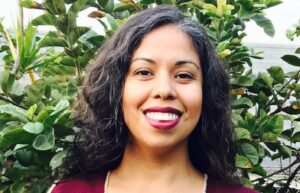 Photo of woman wearing an apron standing in front of a tree.